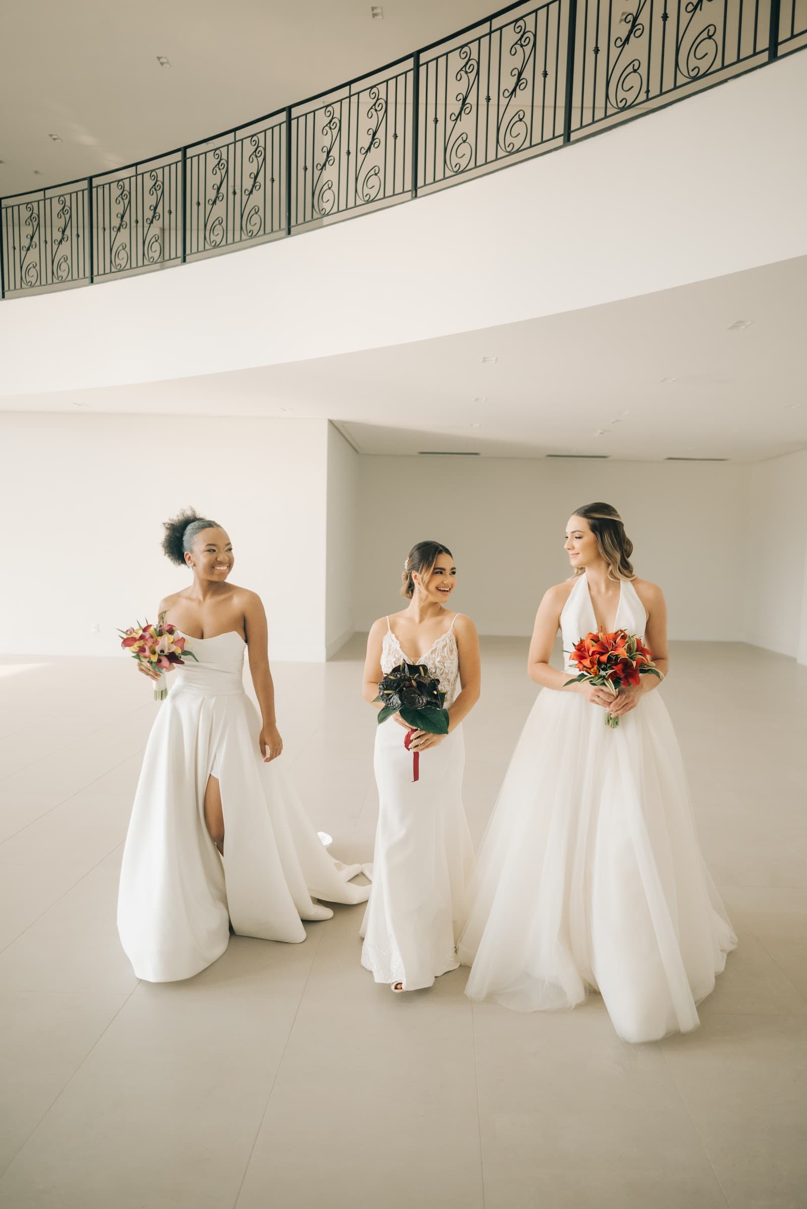 Três noivas de vestido branco e buquê vermelho no salão